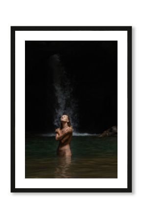 Nude woman embracing solitude in jungle waterfall cave