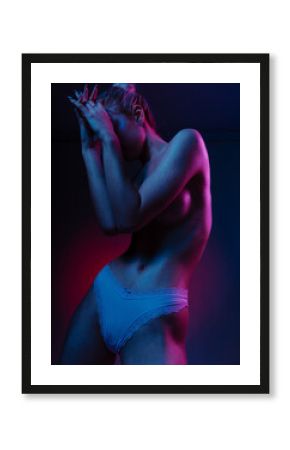 Nude woman in colorful bright neon lights cover breast by hands posing in studio, portrait of beautiful woman touching shoulder body care isolated on colorful glowing background