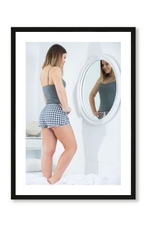 Young sexy woman in pygama using mirror in bedroom in morning