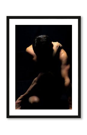 artistic nude male model silhouette pose accenting muscular definition with black background, vertical