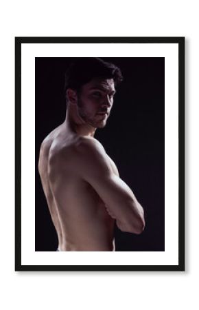 Natural Portrait of Confident Thinking Caucasian Bodybuilder Athlete Man Posing With Naked Torso Looking Backwards Against Dark