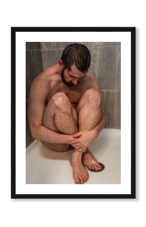 depressed, anxious, or sad man naked sitting in shower legs crossed as water runs over bare skin and face with wedding band visible 