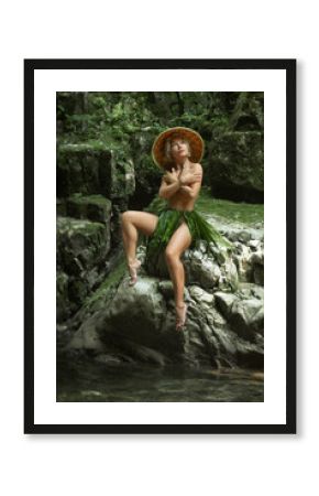 a naked sexy girl in a triangular hat and a homemade cape made of leaves stands at the waterfall of a beautiful mountain river