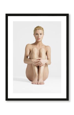 Portrait of a nude young woman sitting with hands on knees against white background