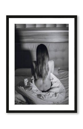 Back view of sexy young naked woman is sitting on white bed. Black and white photo.
