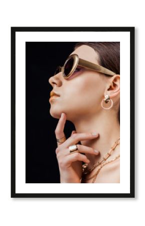 profile of young naked woman in sunglasses, golden earring, rings and necklaces isolated on black