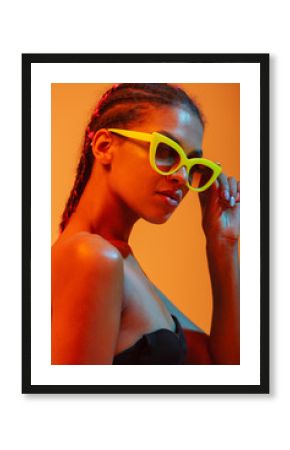 Beautiful young african naked woman posing isolated over yellow neon lights wall background wearing sunglasses.