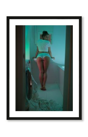 Beautiful sexy lady in white shirt brushing teeth in bathroom. Fashion portrait of model on a bath indoors. Beauty blonde naked woman with attractive body in lingerie. Blue and neon lights background.