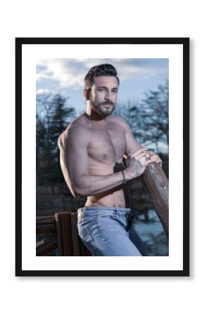 Joven con un tronco de madera. Trabajo en el campo desnudo con el pecho y el abdomen definido del gym tipo firtness. pantalón de mezclilla frente al lago en verano con una iluminación perfecta.