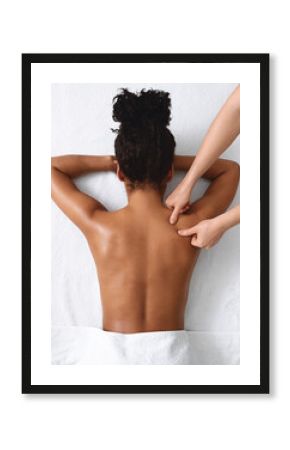 African american naked woman getting relaxing back massage on white, view above. Top view of black lady having healing body massage from unrecognizable female therapist at modern newest spa