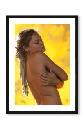 Naked woman with dreadlocks poses, golden light casting a warm glow.
