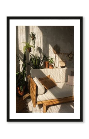 Boho style modern home interior design. Sofa, pillows, home plants, carpet and decorations against concrete wall. Bohemian sitting room with warm sun light shadows on the wall.