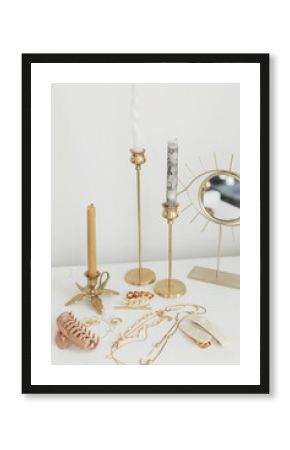 Modern gold jewellery, hair clips on white table with vintage candles and boho mirror. Accessories