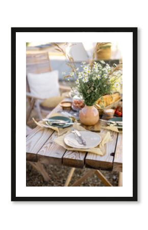 Beautifully served wooden table in natural boho style outdoors. Dining table decorated with field flowers, dishes and fresh food