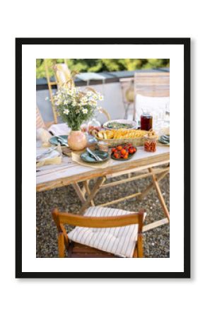 Beautifully served wooden table in natural boho style outdoors. Dining table decorated with field flowers, dishes and fresh food