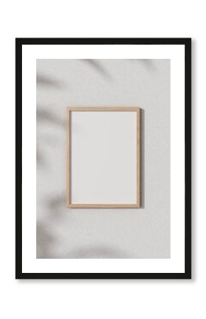 Front view of a wooden picture frame mockup hanging on a white wall with shadow of leaves.