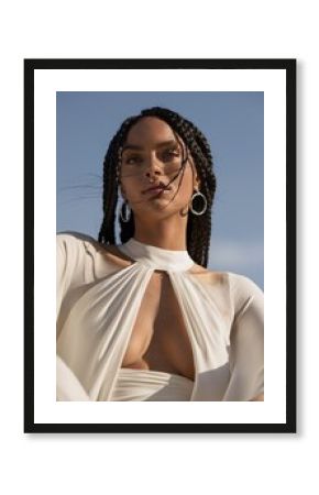 Sun-Kissed Elegance:  A captivating portrait of a  woman with  intricate braided hair against a backdrop of a clear blue sky.  Her confident gaze and  effortless style radiate beauty and power.  The i