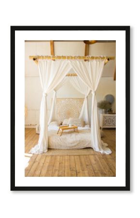 white canopy bed in boho style interior. a white cup stands on a tray on a white bed at morning