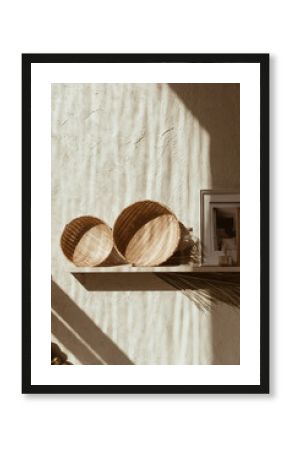 Modern boho style home interior design, Bohemian decoration accessories: photo frames, straw plates on wooden shelf on concrete wall, Warm sunlight silhouette shadows on the wall, Vintage concept,