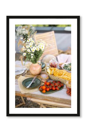 Beautifully served wooden table in natural boho style outdoors. Dining table decorated with field flowers, dishes and fresh food