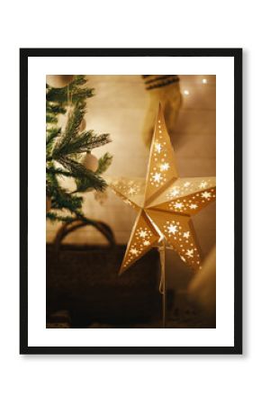 Merry Christmas! Stylish Christmas star, tree with white baubles, boho ornaments, golden lights and gifts in atmospheric evening room. Festive scandinavian room at eve. Magic time. Space for text.