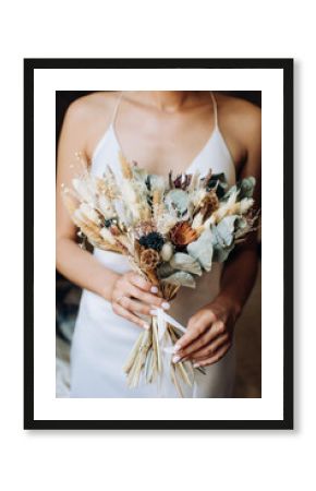 The bride holds in her hands a beautiful bouquet of dried flowers in the style of boho