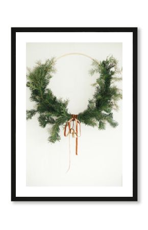 Merry Christmas and Happy Holidays! Modern Christmas wreath with velvet ribbon and golden bells hanging on white wall background. Winter holiday decor, moody image. Boho wreath