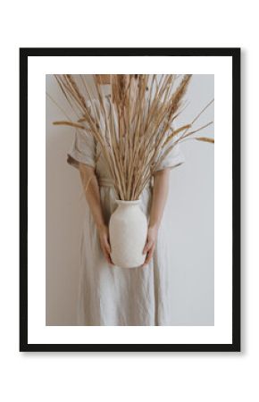 Young beautiful woman in neutral pastel beige linen dress holding sandy earthenware with dried pampas grass. Aesthetic stylish fashion tan beige coloured composition