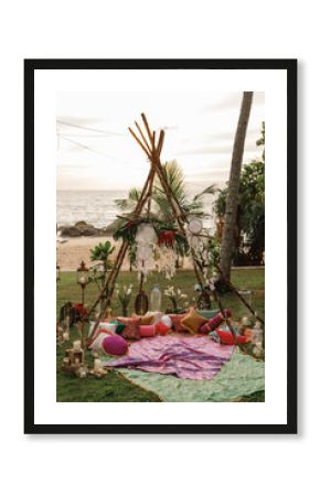 Wooden wigwam decorated with green  branches in the backyard, event or wedding in boho style. beautiful original triangular wooden wedding arch with flowers and greenery in the open air