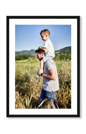 Father carrying son on shoulders while walking amidst plants against clear sky during sunny day