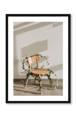 Wooden chair tied with green leafy twigs indoors, on white wall background.