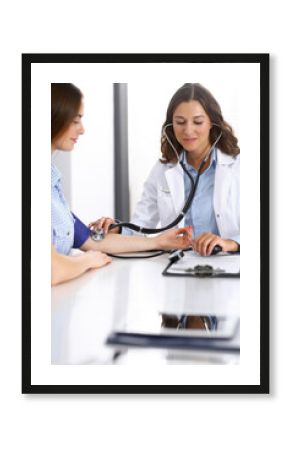 Doctor checking blood pressure of female patient while sitting at the desk in hospital office. Cardiology in medicine and health care concept