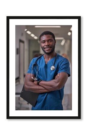 confident afro american nurse posing in hospital hall aisle, take a break during work, wearing blue uniform, smiling. medicine and health concept