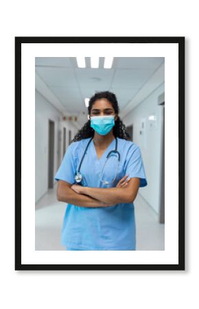 Portrait of mixed race female doctor wearing face mask standing in hospital corridor