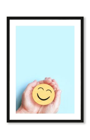 Hand holding happy smile face on blue background, Positive thinking, Mental health, World mental health day concept.