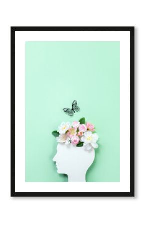 Cardboard silhouette of human head decorated with flowers and butterfly on mint background. World mental health day concept. Vertical banner. Copy space