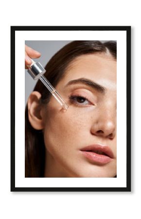 close up of young Caucasian woman with brunette hair and clean skin applying serum with cosmetic pipette