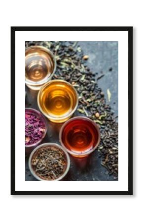 Several cups of tea are arranged on a table with loose tea.  Vertical background 