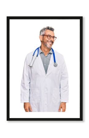 Middle age grey-haired man wearing doctor uniform and stethoscope looking away to side with smile on face, natural expression. laughing confident.