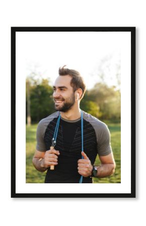 Handsome young strong sports man posing outdoors at the nature park location with skipping rope.