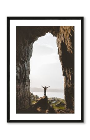 Man standing alone in cave Travel adventure vacations happy raised hands tourist success wellness concept Kirkehelleren grotto in Norway