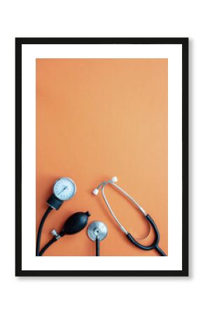 Medical stethoscope and sphygmomanometer on orange background, top view.