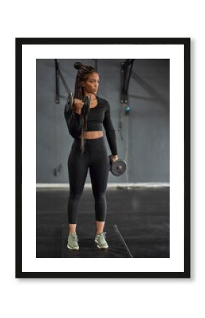 Confident female athlete with braided hair lifting dumbbells in health club