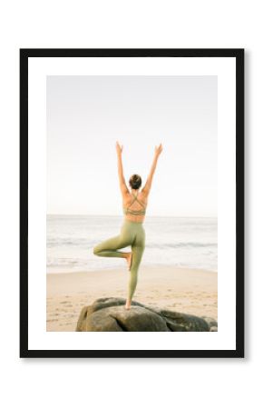 Woman practicing yoga tree pose on rock at beach