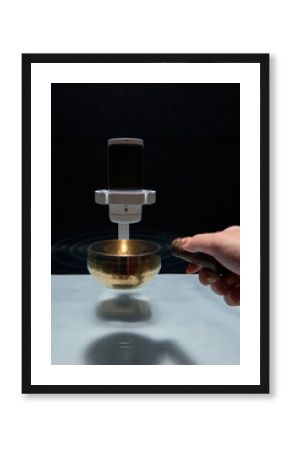 Professional microphone recording the healing sound waves from a glowing Tibetan singing bowl during a therapy session.