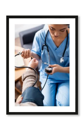 young asian woman measuring blood pressure of elderly woman with tonometer, blurred foreground