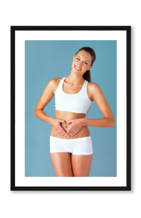 Heart shape, hand gesture on stomach and happy woman in portrait, gut health and wellness isolated on blue background. Weight loss, fitness and healthy female person, self love and bodycare in studio