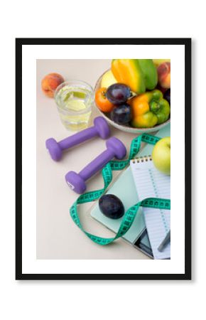 The concept of a healthy lifestyle, sports, fitness, healthy nutrition, daily routine. A plate with vegetables and fruits, scales, dumbbells, a centimeter, a clock on a light background.