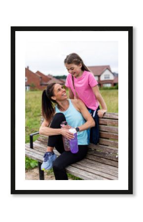 Playful daughter with mother holding water bottles sitting on bench