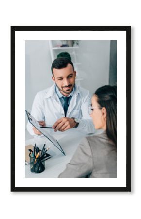 cheerful doctor pointing on insurance claim form to patient in clinic